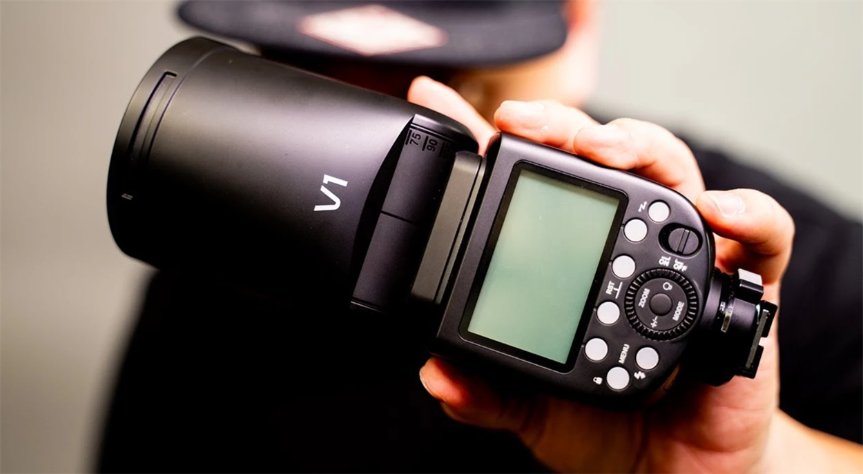 Задня панель спалаху Godox V1 у руках фотографа з монохромним LCD-екраном та диском управління налаштуваннями.
